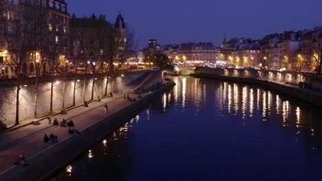 Paris-famous-Quais-de-Seine-river-bank-by-night-with-lights-and-people,-wide-panning-shot