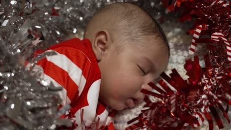 adorable cute 2 month old indian baby boy sleeping surrounded by red and silver tinsel