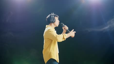 side view of young asian boy with headphone holding a microphone and rapping on the white smoke black background