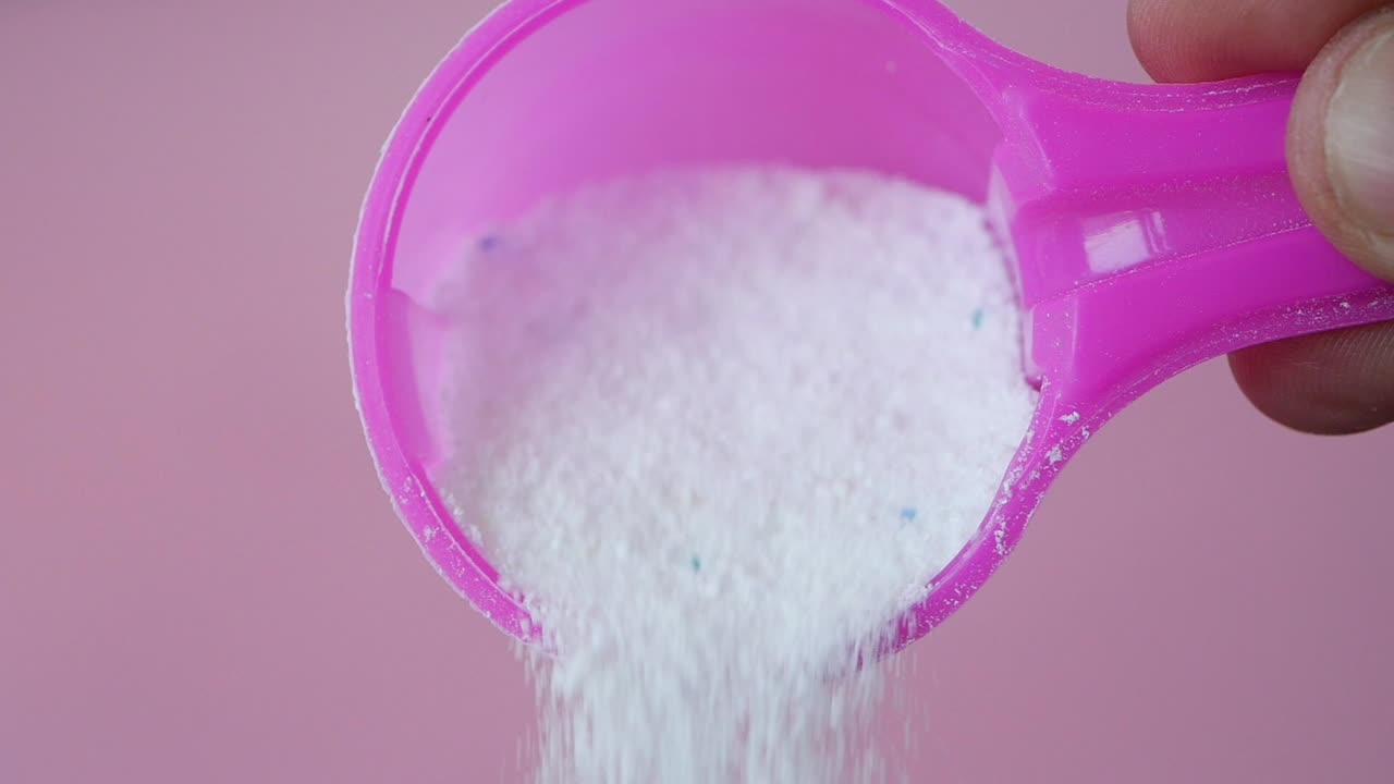 una cuchara de detergente para la lavandería saliendo de una cuchara rosada