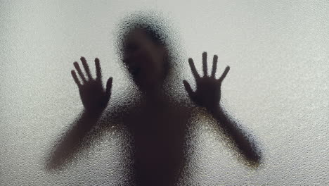 a female silhouette behind the frosted glass moves slowly and screems