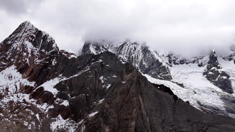 cinematic aerial view of snowy andes mountains in peru with glaciers, rocky cliffs, and hidden blue alpine lake under misty clouds, dramatic landscape and natural travel destination