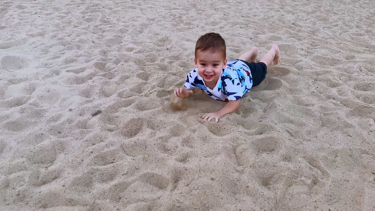 Cute lovely toddler crawling by the white sand outdoors. Happy kid lies down on the sand and having rest.