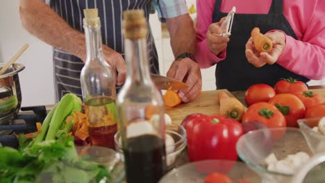 mid section of diverse senior couple wearing aprons and cooking in kitchen