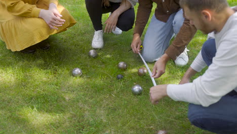 close-up view of a group of men and women friends calculating distance between petanque balls in the park