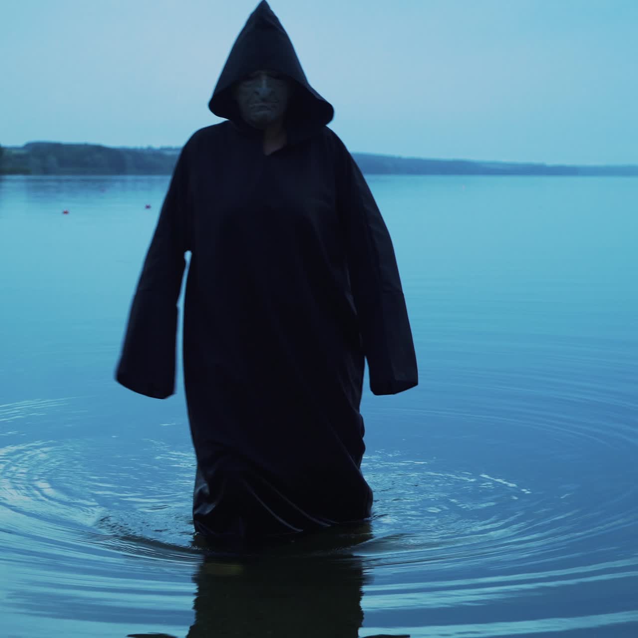 Evil witch in black cloak with hood in the river. Halloween costume.