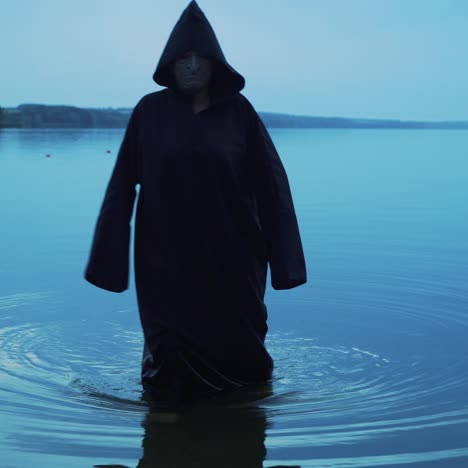 evil witch in black cloak with hood in the river. halloween costume.