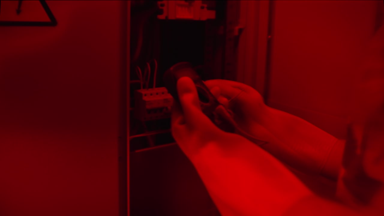 electricista trabajando en un panel eléctrico en un entorno de luz roja