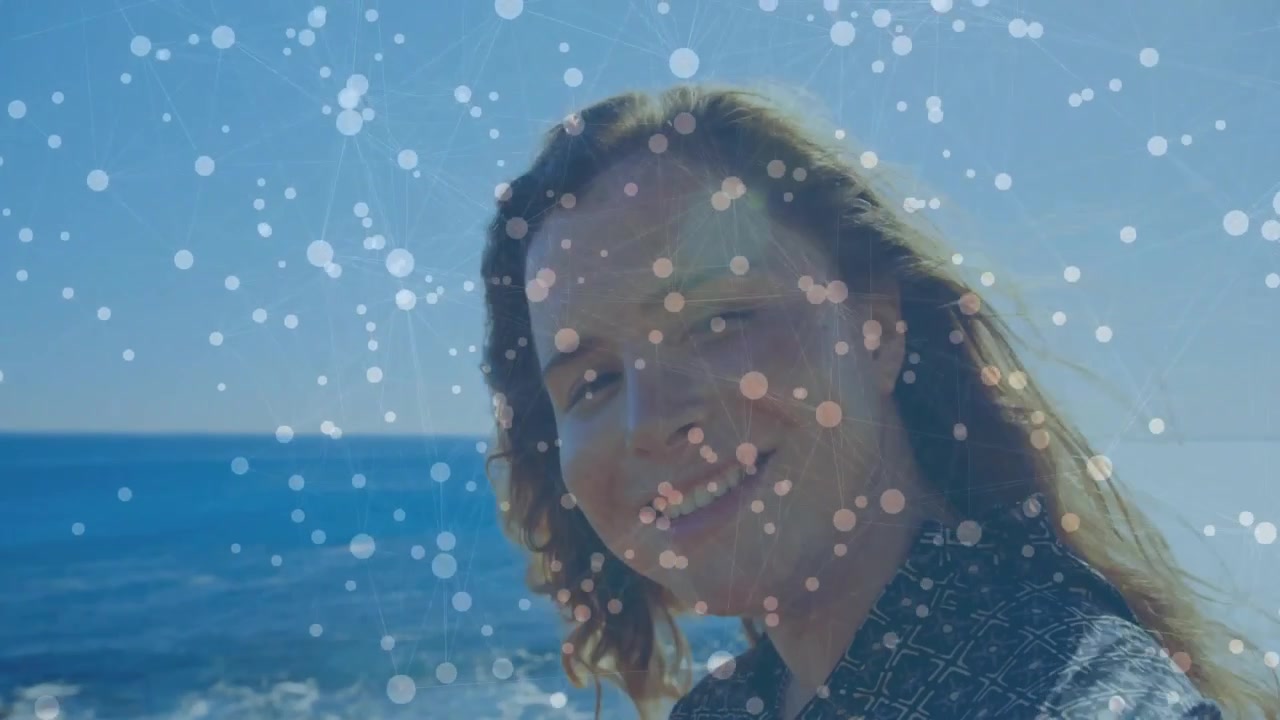 Smilende kvinne iført mørk skjorte snur hodet ved strandkanten med hav, solblending, bokeh, kopieringsplass