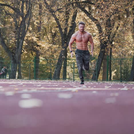 healthy athlete is running in the stadium. young sportsman is involved in sport running on the autumn trees background. view from below.