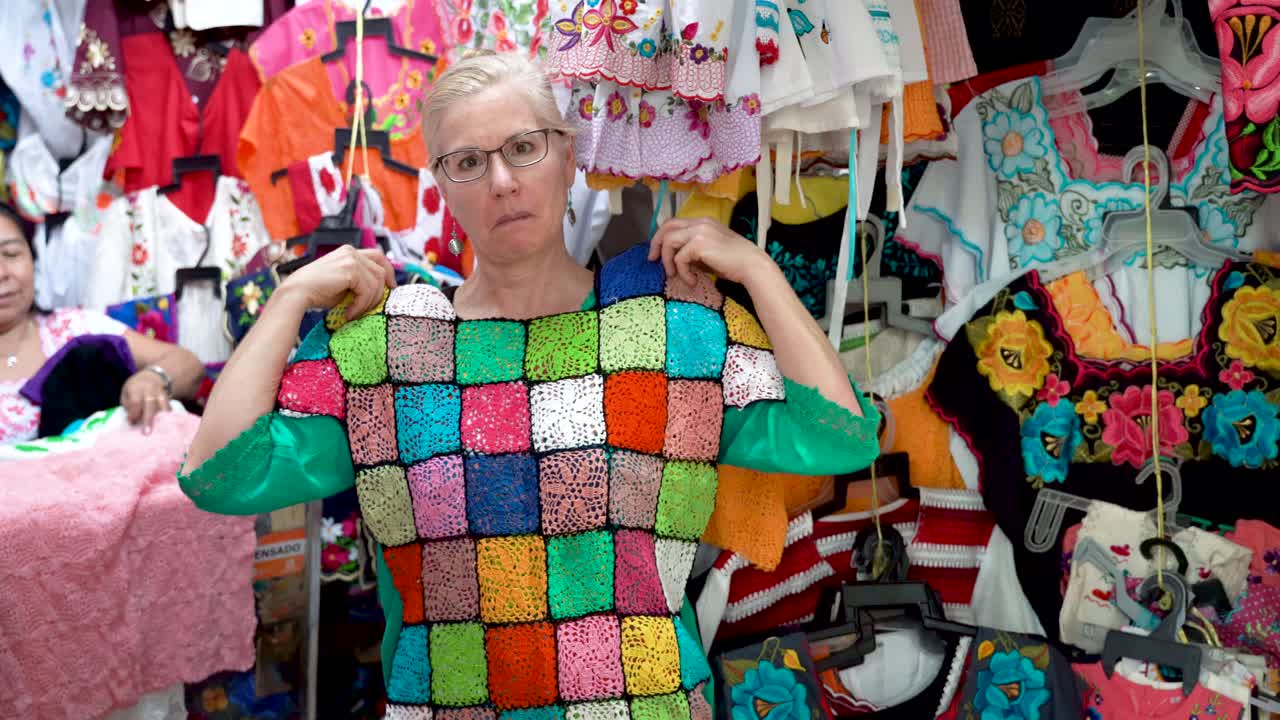 una mujer madura sostiene una colorida blusa de crochet mexicana y pregunta: "¿te gusta?" y sonríe en mérida, méxico