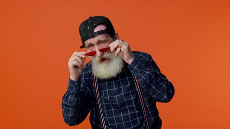 Playful-happy-elderly-bearded-man-in-sunglasses-and-cap-blinking-eye,-looking-at-camera-with-smile