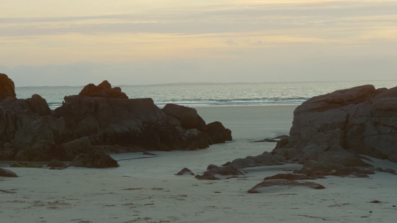 pequeñas rocas en la playa con el océano en el fondo al atardecer