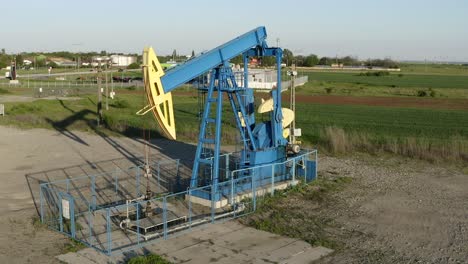 Aerial:-old-oil-pump-rig-in-countryside,-pulley-extracting-oil-from-ground