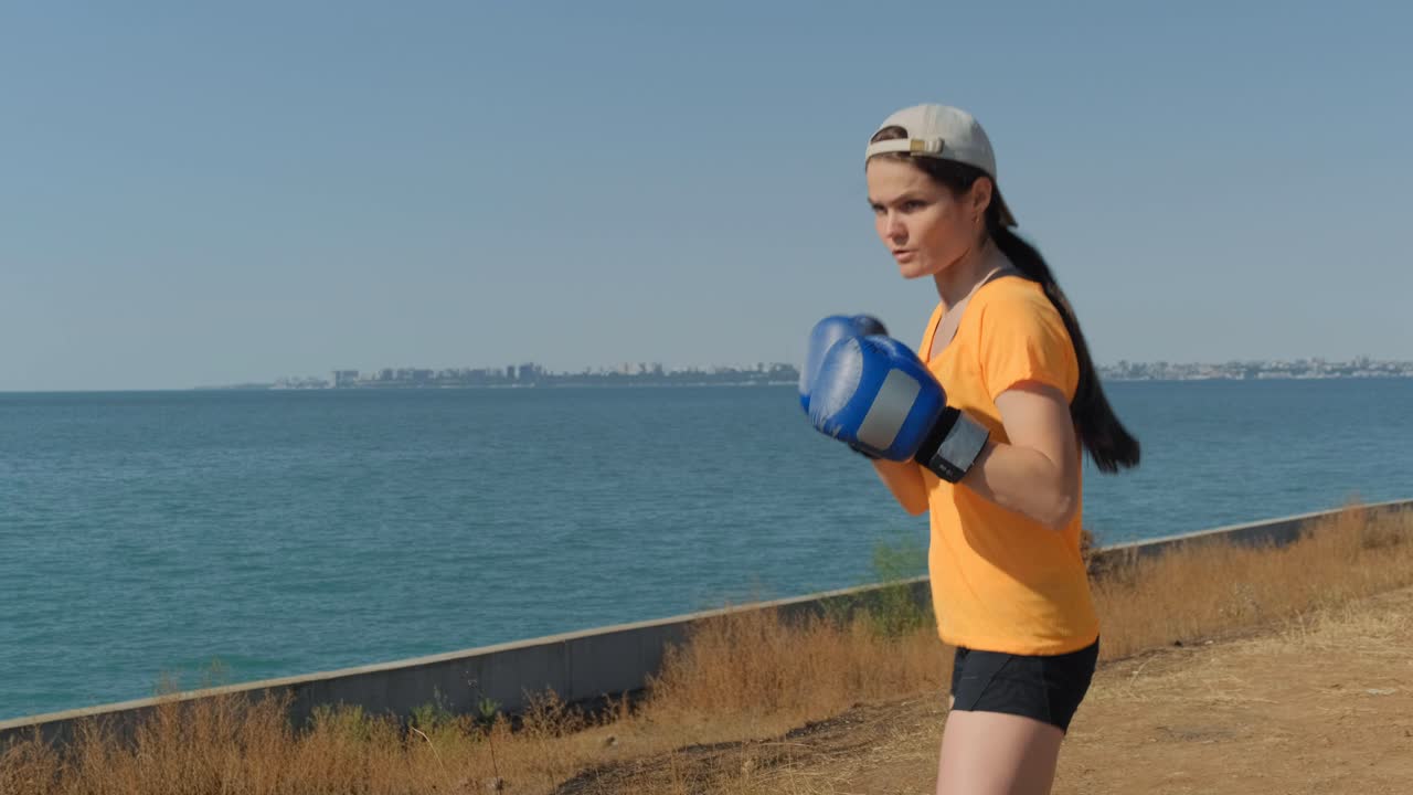 Young woman practicing boxing with gloves on the seashore in the evening without a punch bag