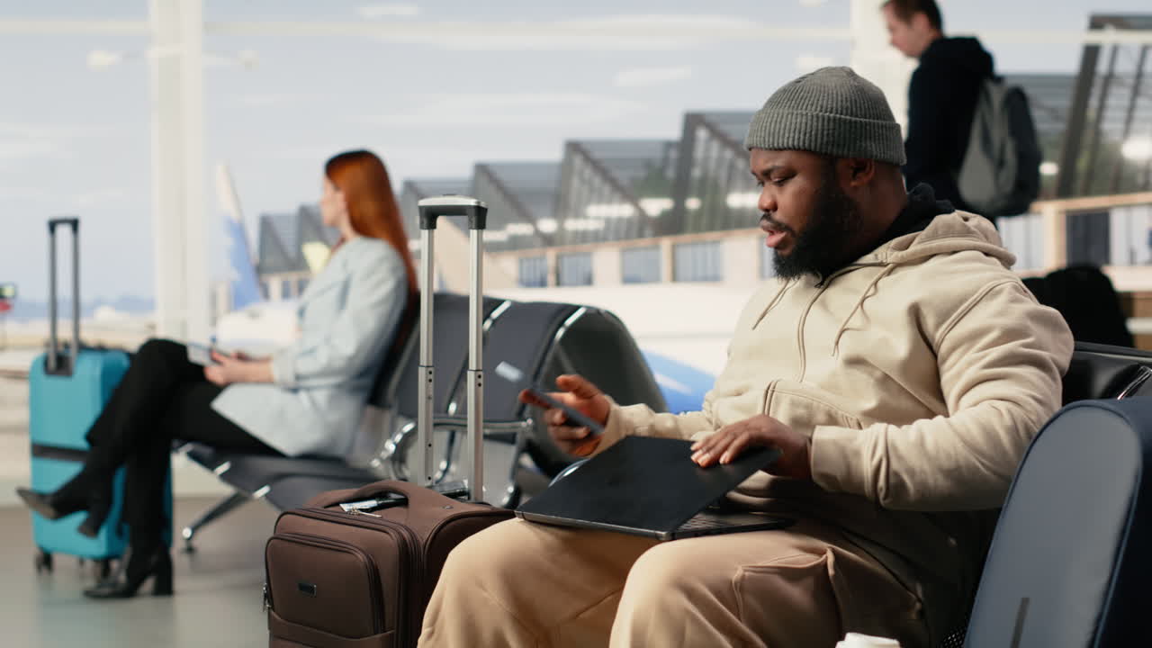 Man Using Laptop and Phone While Waiting in Airport Terminal