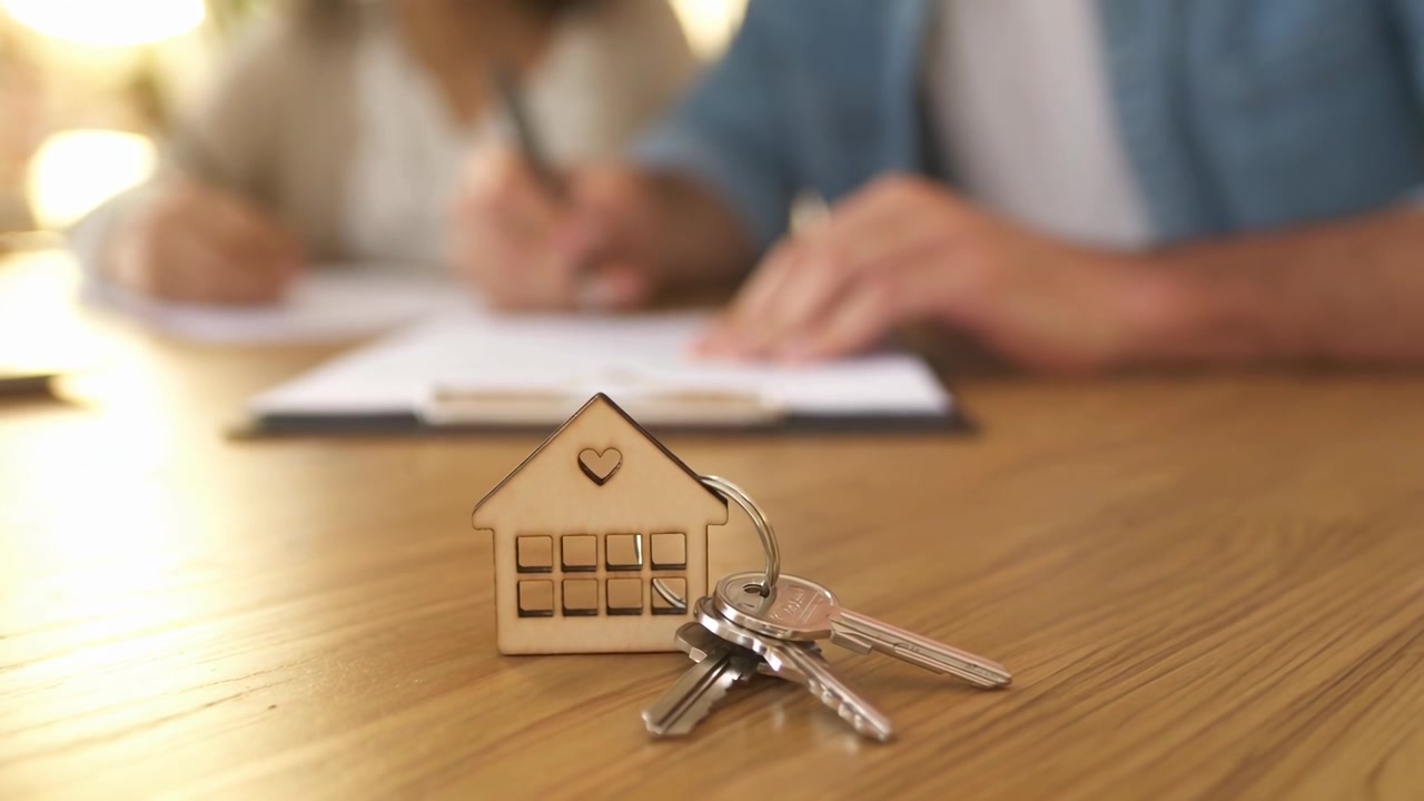Pareja firmando un contrato inmobiliario con las llaves de la casa sobre la mesa