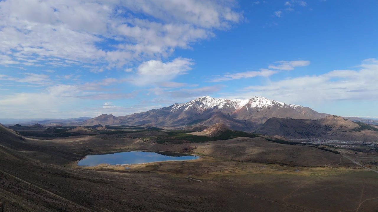 Sereno lago laguna Willimanco a Esquel, Chubut, immerso tra dolci colline e le Ande innevate in lontananza, che attira escursionisti e appassionati della natura, ripresa aerea in slow motion