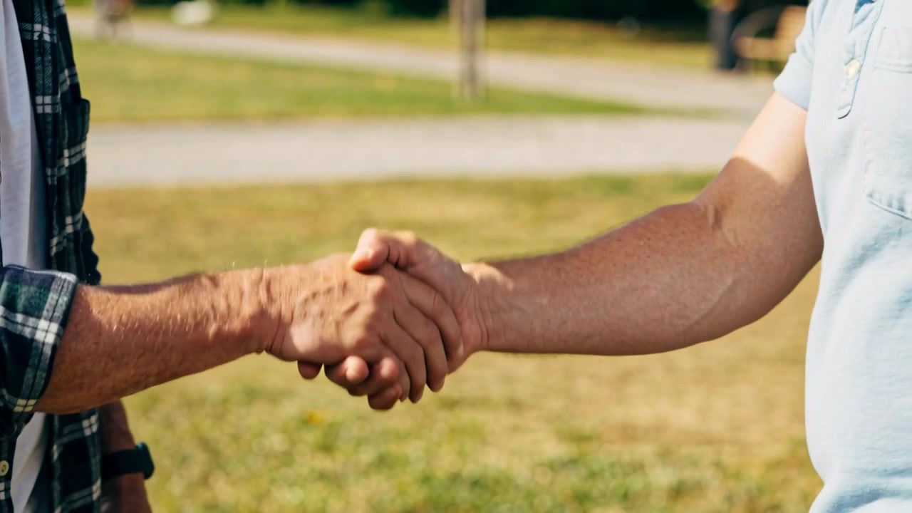 L'uomo a destra stringe la mano in un saluto fermo al parco, con uno smartwatch.