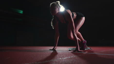 Una-Joven-Atleta-Delgada-Está-En-Posición-De-Comenzar-A-Correr-En-Las-Almohadillas-De-La-Pista-En-Cámara-Lenta