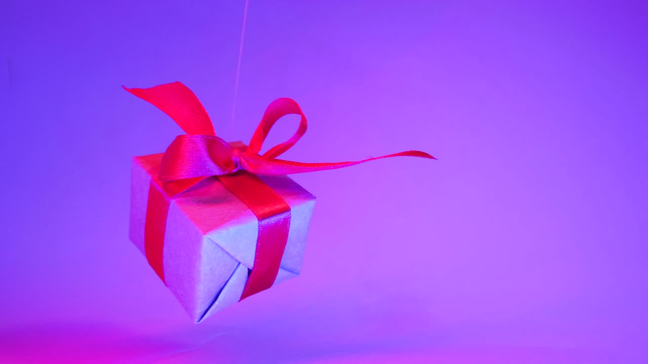 caja de regalos con cinta roja se balancea de un lado a otro en el fondo púrpura de neón de moda. gravedad cero. levitación. ventas de concepto, precio de descuento, vacaciones de navidad y compras