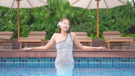 a young woman stands in the shallow end of a resort swimming pool leans along the edge of the pool