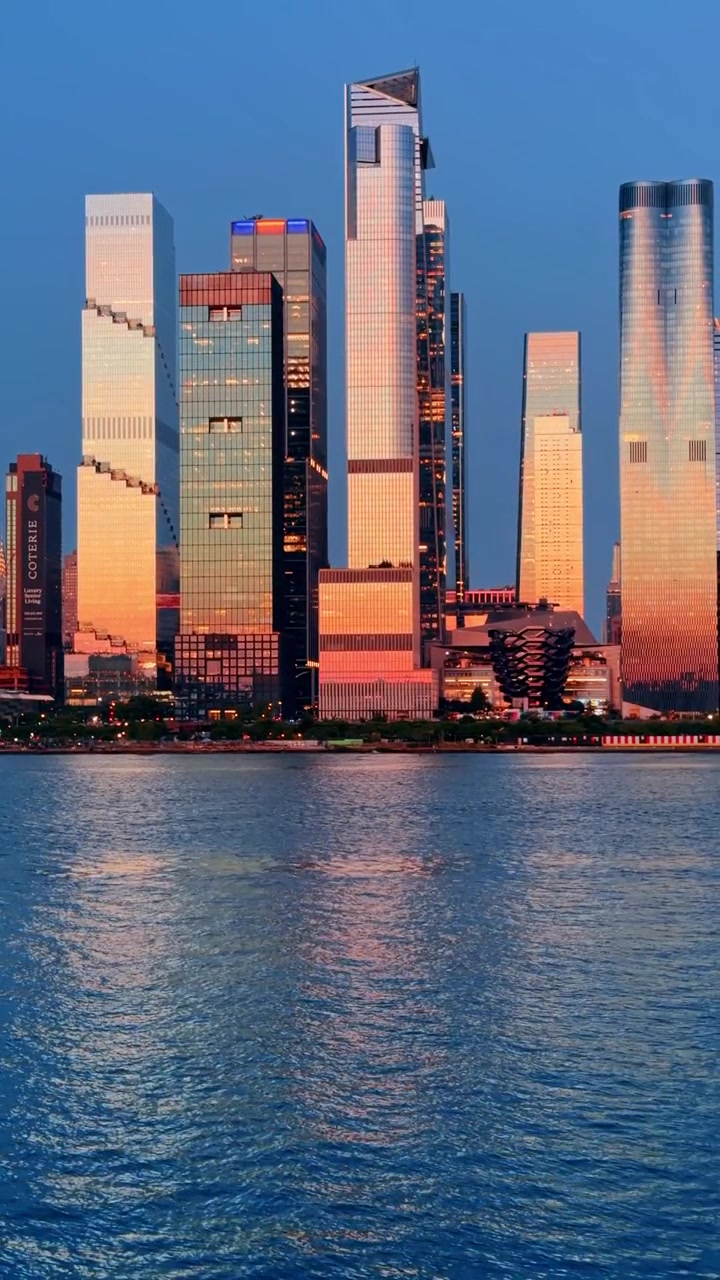 New York, USA, 22. mai 2026: Hudson Yards-tårnene reflektert i elven i blåtimen, Manhattan. Glasskyskrapere med varm fasadeglød og bikakestruktur på rolig dypt blått vann.