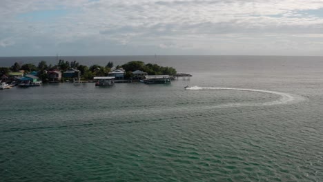 Jet-Ski-navigates-waters,-island-sea-landscape,-houses-of-Utila-Honduras,-Aerial