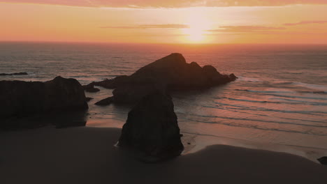 Drone-flying-forwards-over-a-beautiful-beach-and-silhouetted-sea-stacks