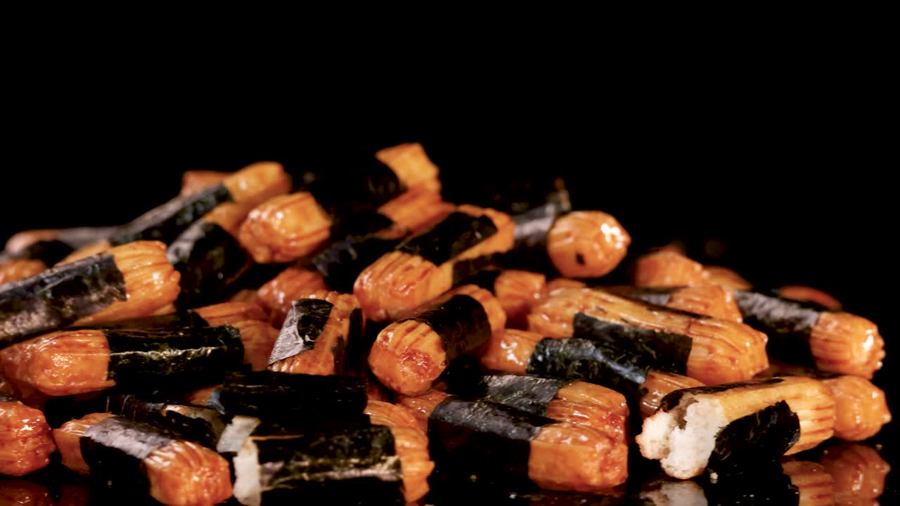 Hand picks crunchy Japanese rice crackers from pile, close-up, black background, dramatic lighting