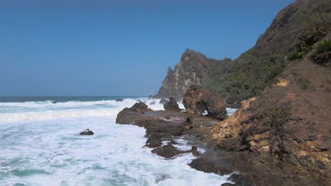 Rocky-mountains-and-foamy-ocean-waves-hitting-coast,-aerial-view