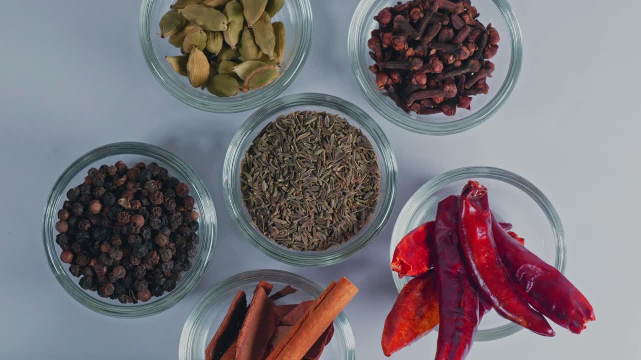 top view of multiple indian whole spices in small glass bowls spinning in round table, slow motion, 4k