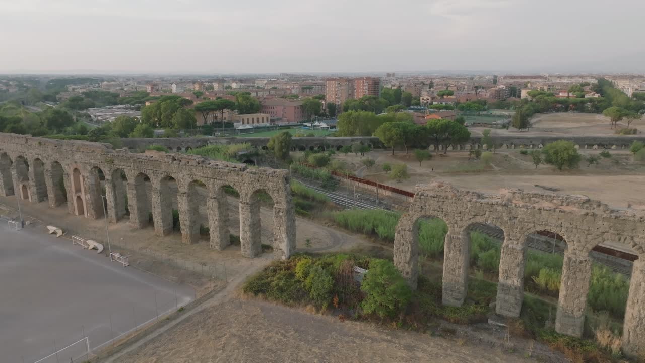 An aerial shot of an Italian aqueduct with a city in the background. The drone moves away from the aqueduct, revealing more of the surrounding landscape.