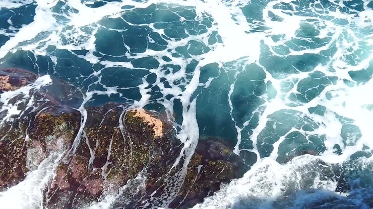 HD Hawaii Kauai: Zeitlupenaufnahme von sich wirbelnden und brechenden Meereswellen, die Felsen im unteren linken Bildrand bedecken