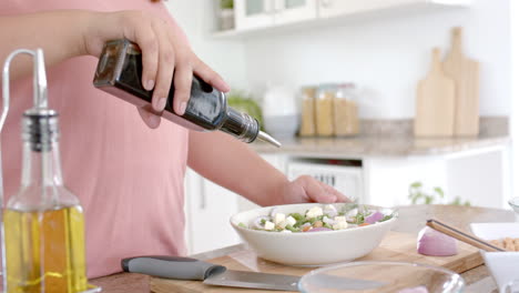midsection of plus size biracial woman dressing salad with vinegar, copy space, slow motion