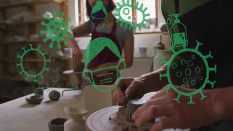 Animation-of-virus-icons-over-diverse-workers-with-face-masks-forming-pottery