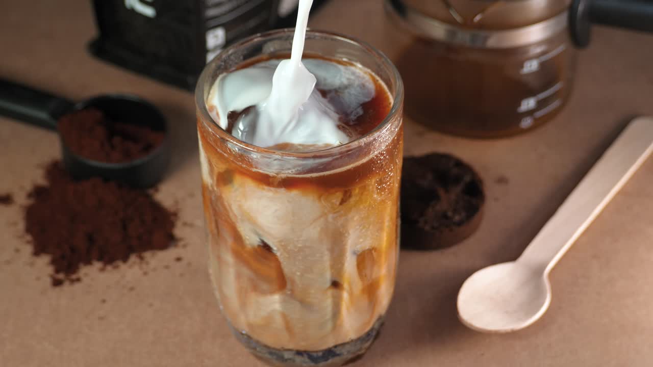Iced coffee drink with milk poured over ice cubes and coffee, on a wooden surface