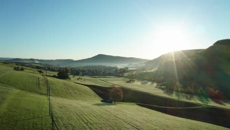 aerial view over agricultural fields during morning sun in the countryside of switzerland, peaceful relaxing drone shot with sun covered sky