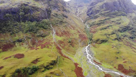 Vista-Aérea-Del-Pintoresco-Paisaje-Montañoso-De-Glencoe-Con-El-Río-Corriendo-Hacia-Abajo