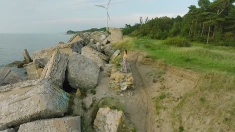 aerial establishing view of beautiful young romantic caucasian girl in a long dress on the white sand beach with old ruins, sunny summer evening, sunset, golden hour, wide drone orbit shot