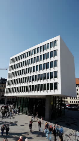 people walking near a modern city building entrance on a sunny day