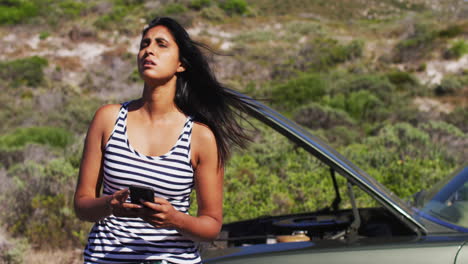 mujer afroamericana usando un teléfono inteligente mientras estaba de pie cerca de su coche averiado en la carretera