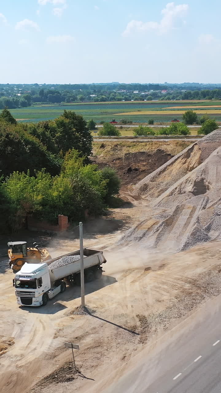Heavy machinery with stones. New road with moving transport near the piles with stones. Trucks loading granite stones. Aerial shot. Vertical video