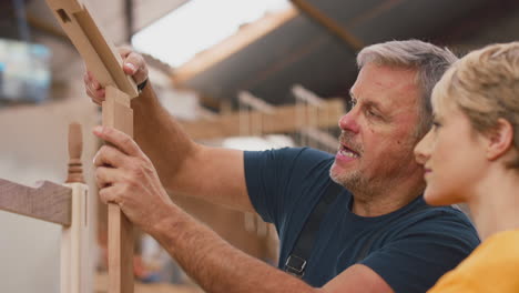 close up of female apprentice learning skills from mature male carpenter in furniture workshop