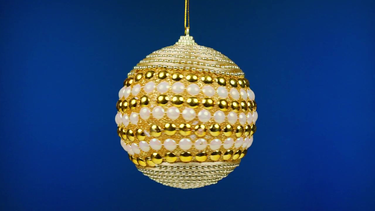 Elegant guld og hvid julekugle roterende på blå baggrund