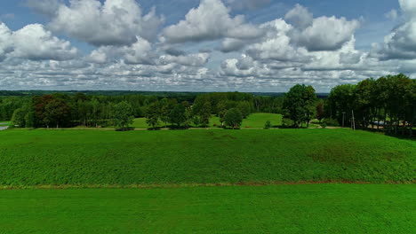 dron aéreo en movimiento hacia atrás sobre tierras de cultivo verdes junto con balas de heno esparcidas en el campo con nubes blancas pasando