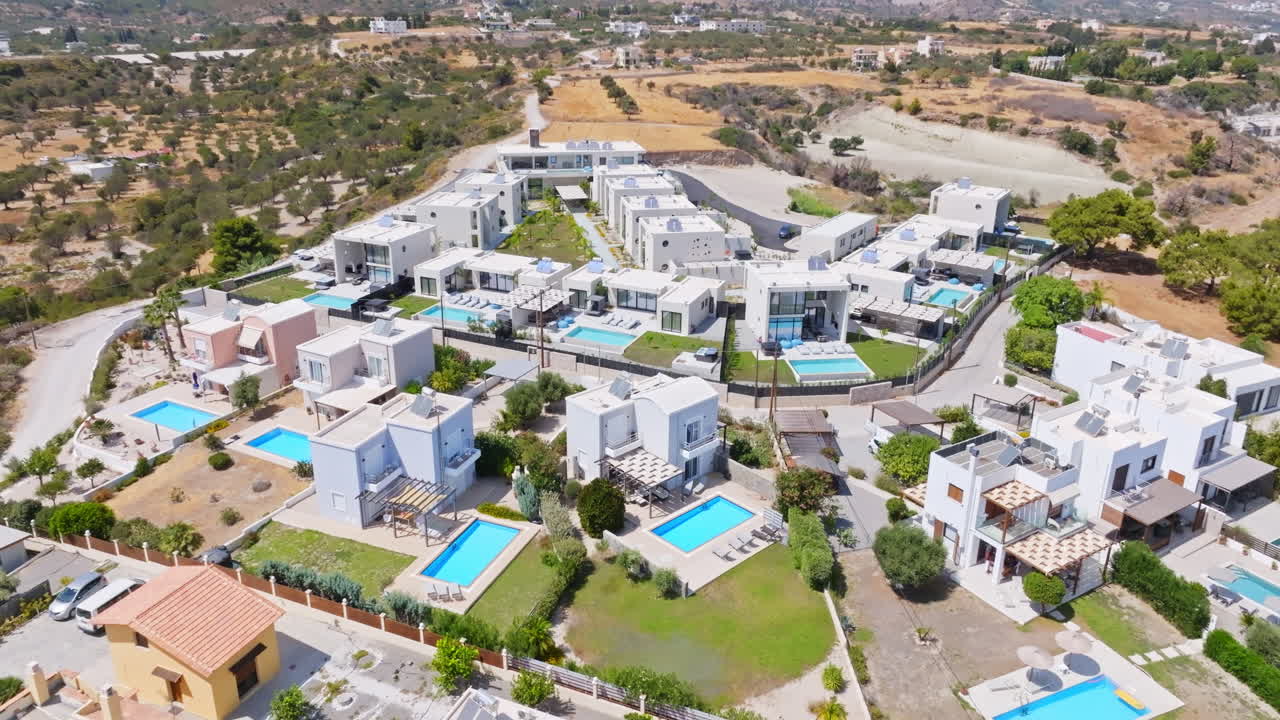 Aerial view rising around a hilltop holiday house village, sunny day in Greece
