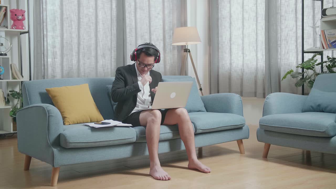 집에서 노트북으로 일하면서 헤드폰으로 음악을 듣고 춤을 추는 재과 쇼트를 입은 아시아 사업가