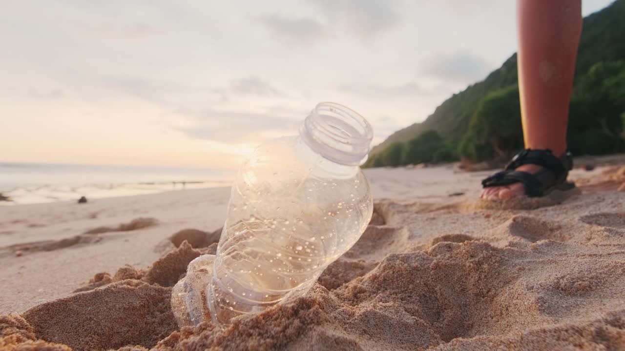 여성 자원봉사자는 해변의 모래에서 플라스틱 병과 컵을 손으로 수집합니다.
