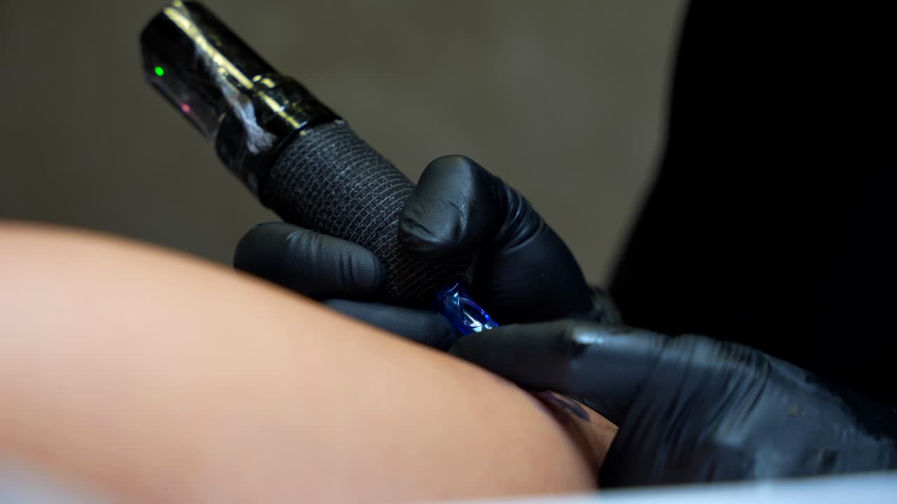 Tattoo artist inks a design on skin using a tattoo machine. Close-up handheld shot